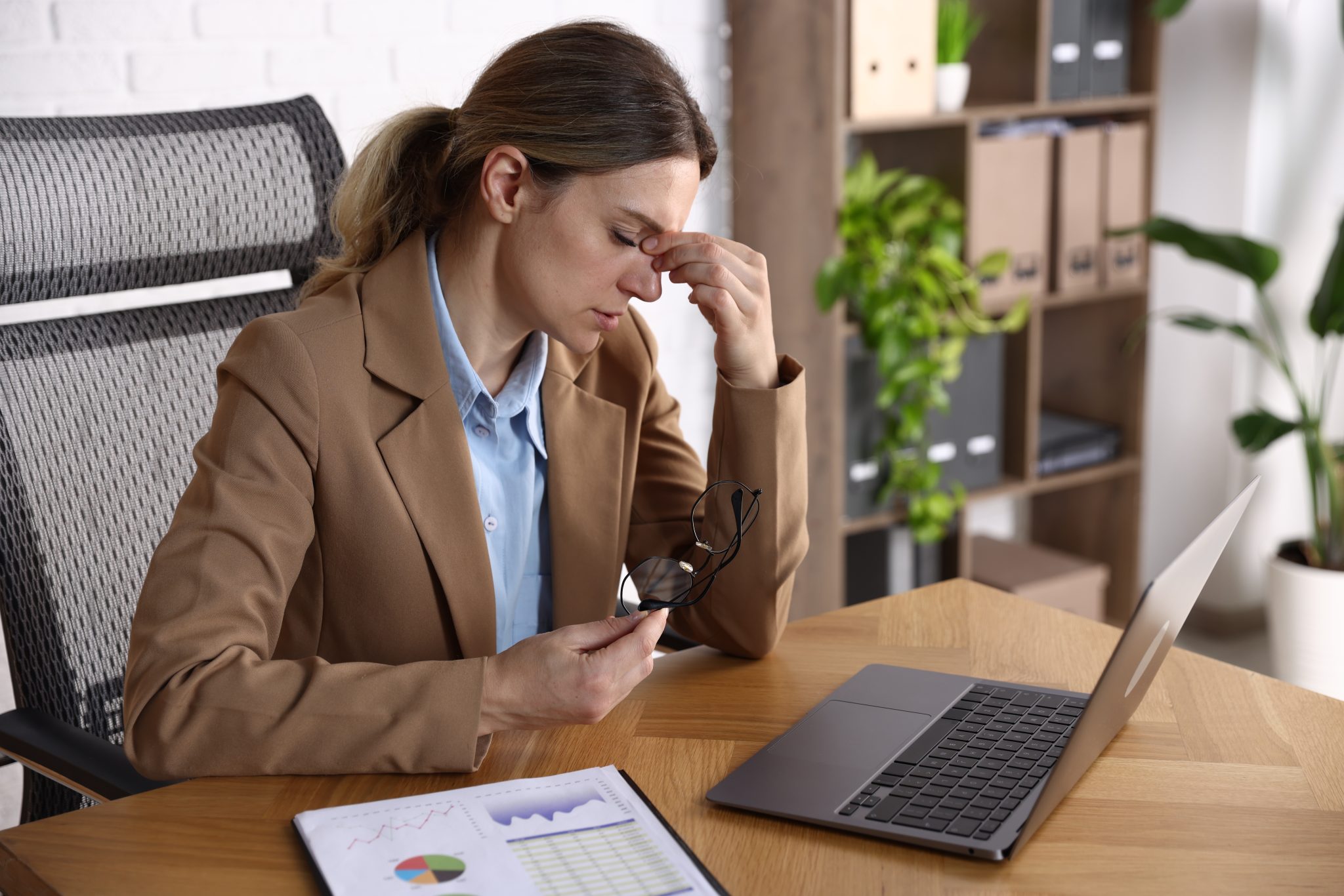 Woman at her desk pinching the bridge of her nose, worried about her parent's care: the hidden cost of the great wealth transfer.